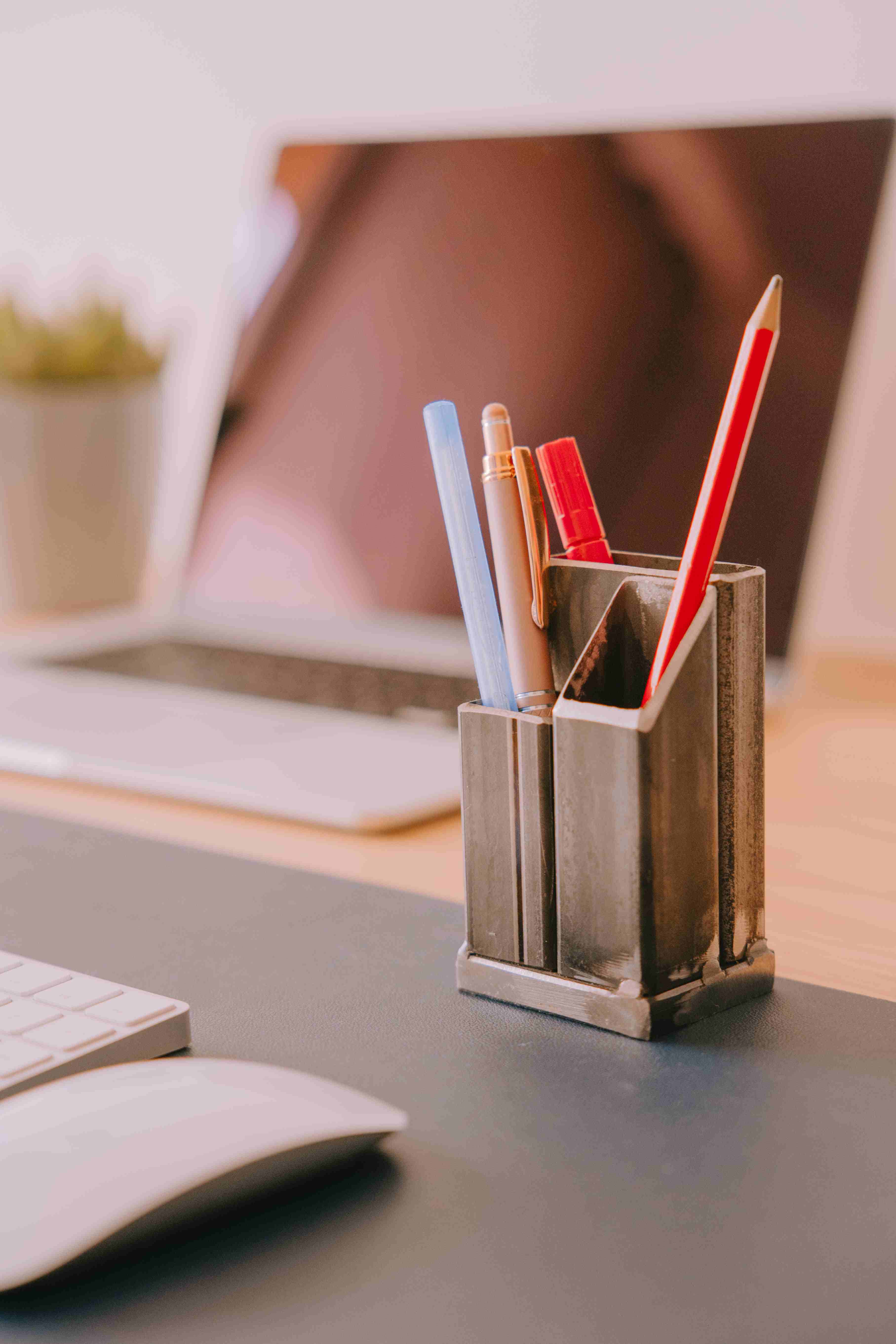 Matt black steel pen holder with pens, pencils and scissors inside on a desk.